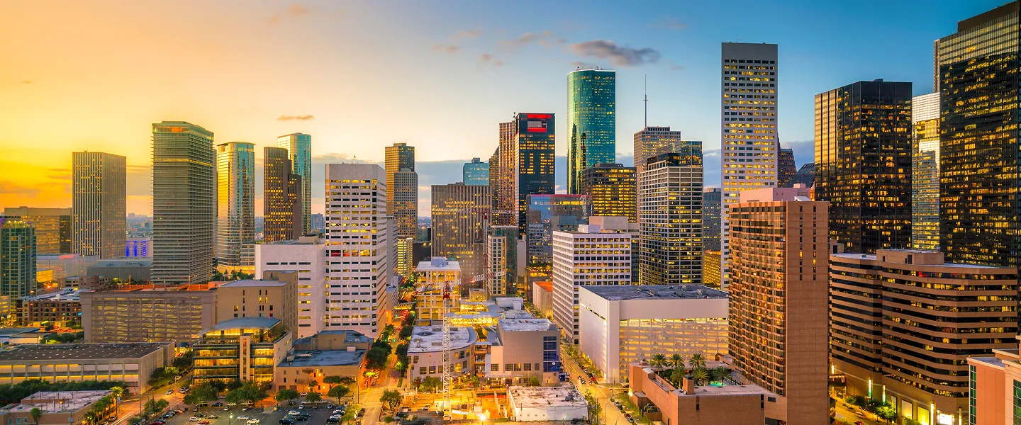 Panoramic view of a modern city skyline at sunset with illuminated skyscrapers.