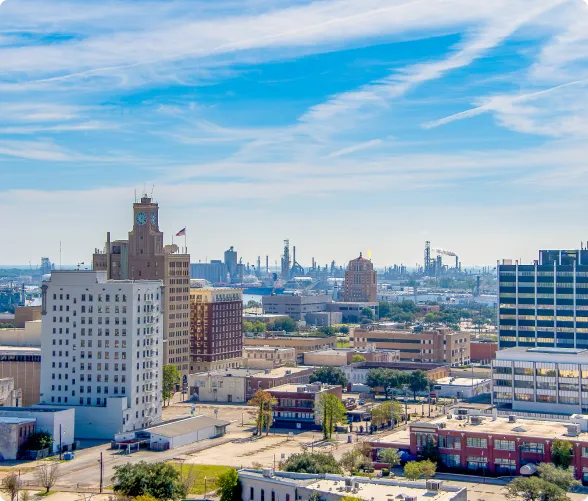 Cityscape featuring mid-rise buildings under a blue sky with wispy clouds.