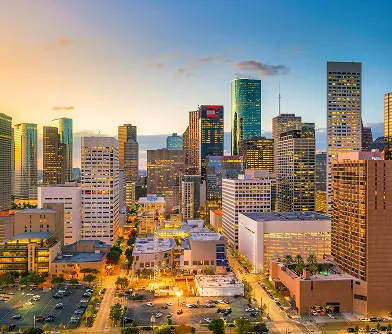 Aerial view of a city skyline at sunset with illuminated buildings and streets.