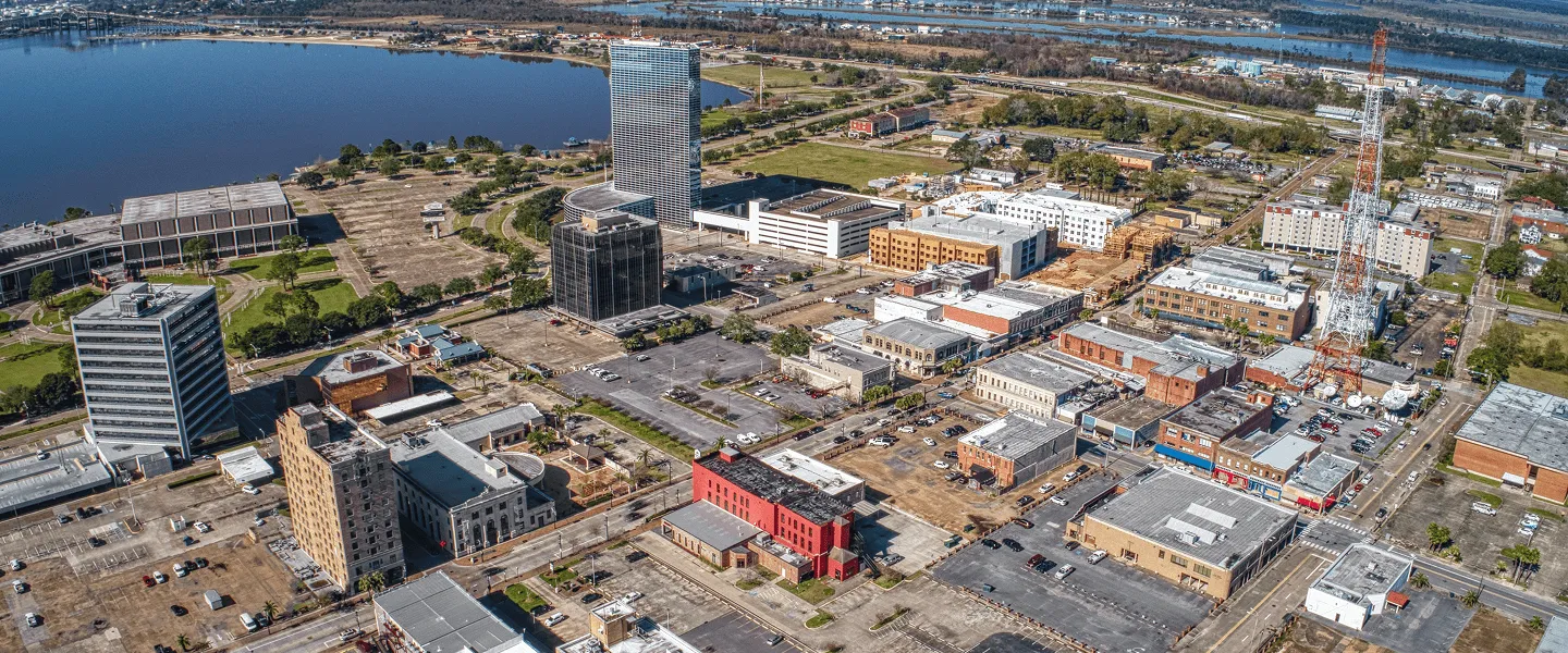Aerial view of urban cityscape with mid-rise buildings, parking lots, river, and communication tower.