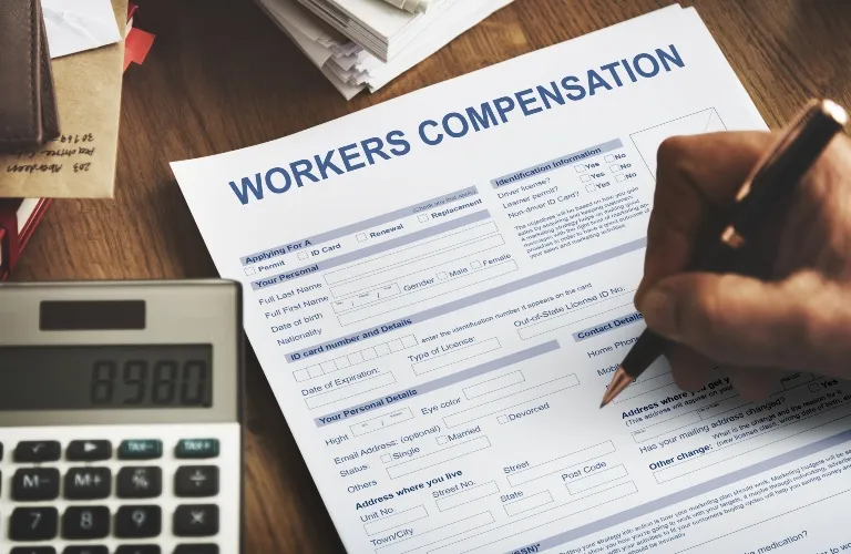 Person filling out a blue and white workers compensation form with a calculator nearby.