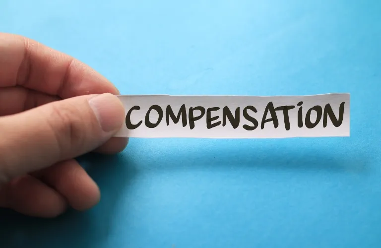 Hand holding a white paper strip with the word "COMPENSATION" written in bold black letters against a blue background.
